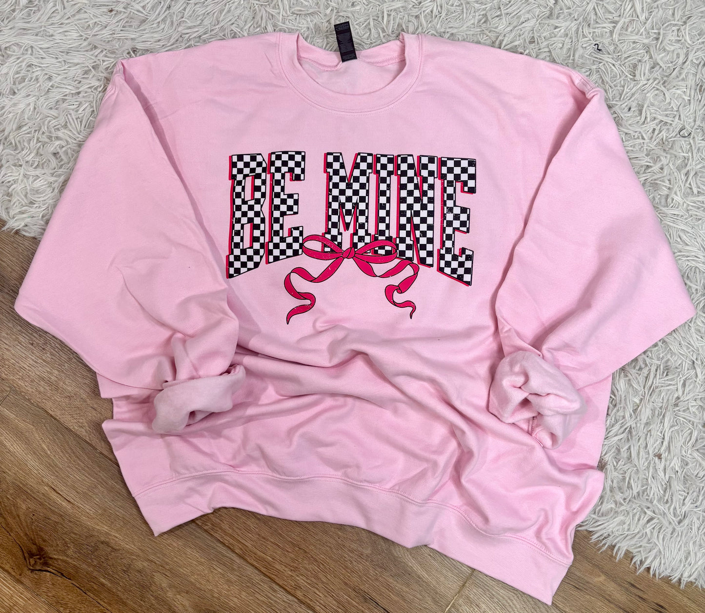 Pink sweatshirt with text and a bow graphic on a textured surface