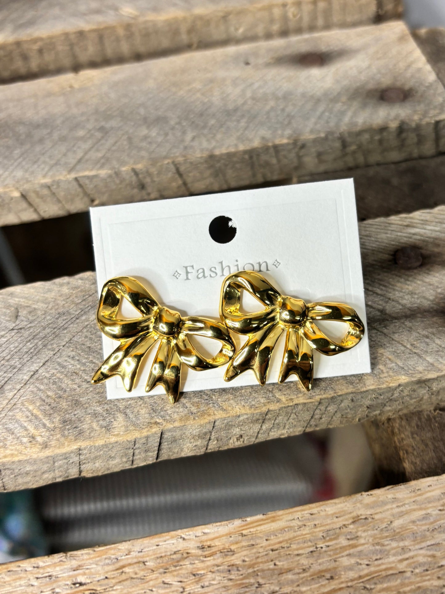 Gold bow-shaped earrings on a white card against a wooden background