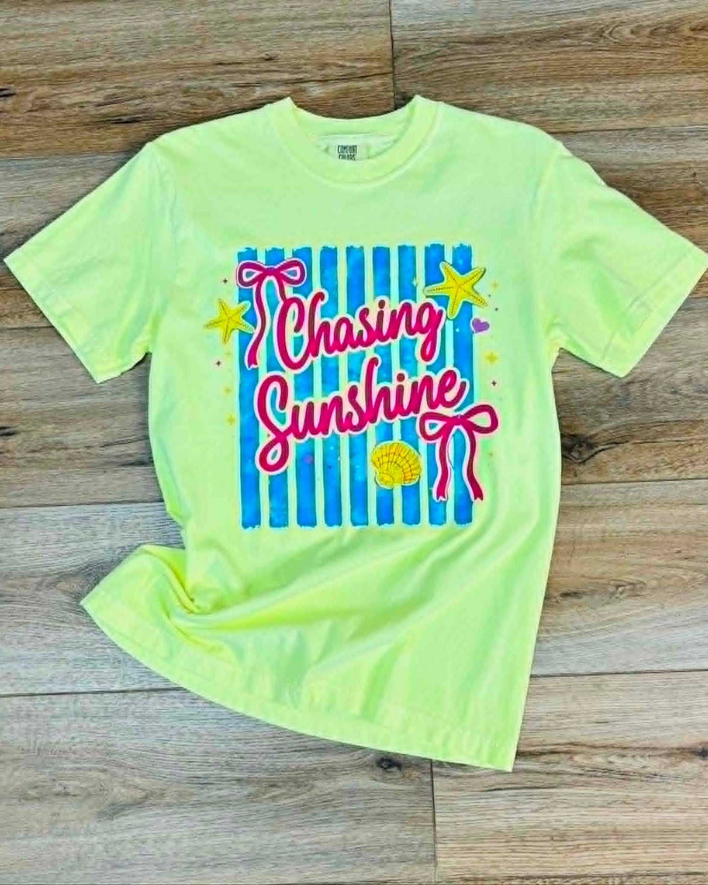 Neon green t-shirt with 'Chasing Sunshine' text on a wooden surface