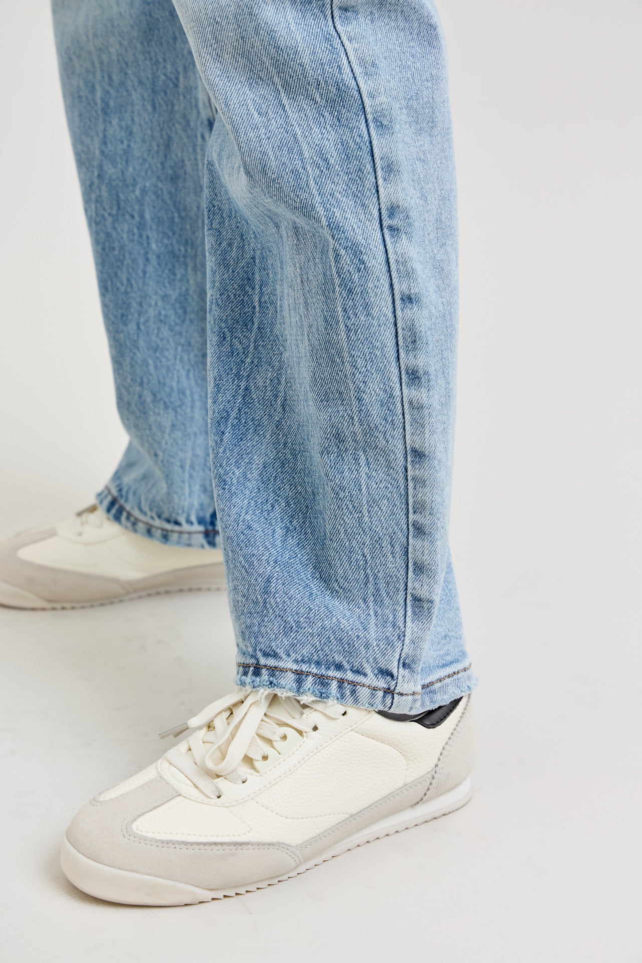 Close-up of light blue jeans and white sneakers on a plain background