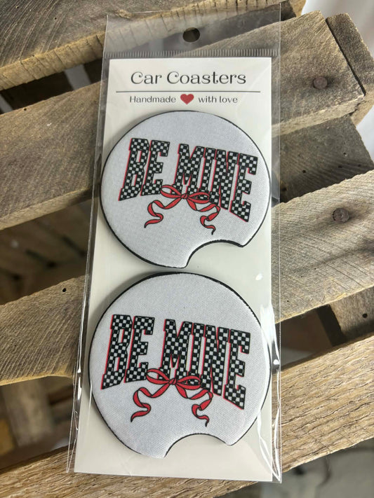 Packaged car coasters with 'BE MINE' text and red bow design on a wooden surface.