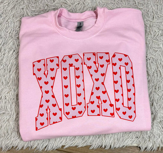 Pink sweatshirt with 'XOXO' design on a textured surface