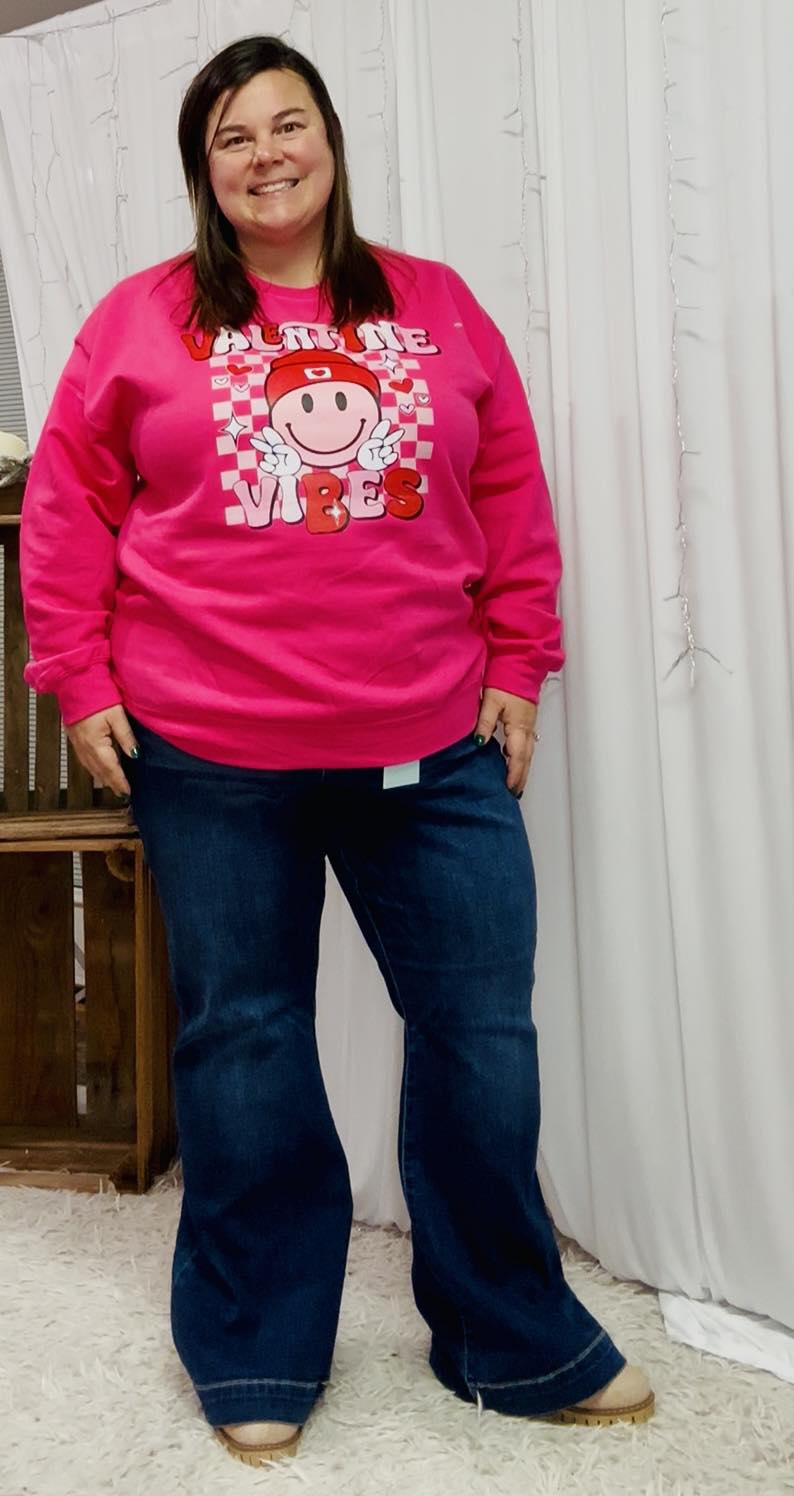 Person wearing a bright pink sweatshirt with a graphic design and blue jeans indoors.