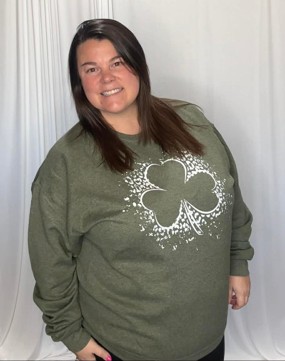Person wearing a green sweatshirt with a white shamrock design against a white curtain background