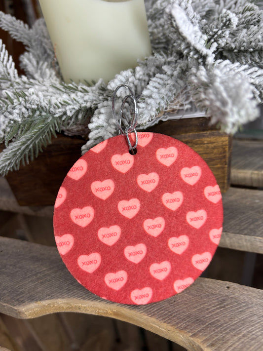 Red circular tag with pink hearts and text attached to a decorative wreath.