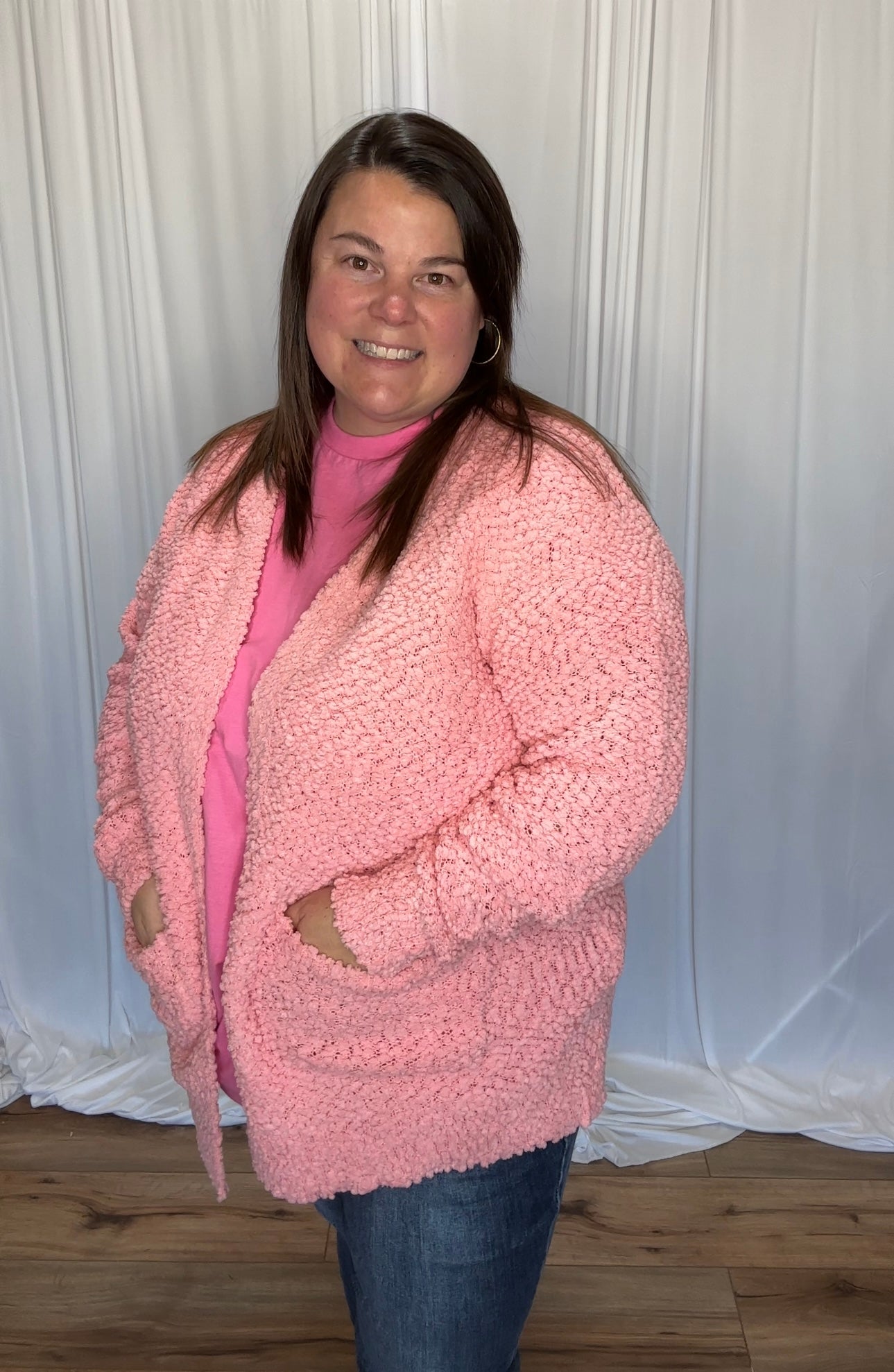 Woman wearing a pink fuzzy cardigan against a white curtain background