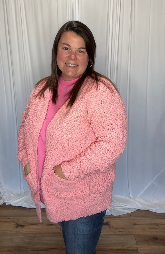 Woman wearing a pink fuzzy cardigan against a white curtain background