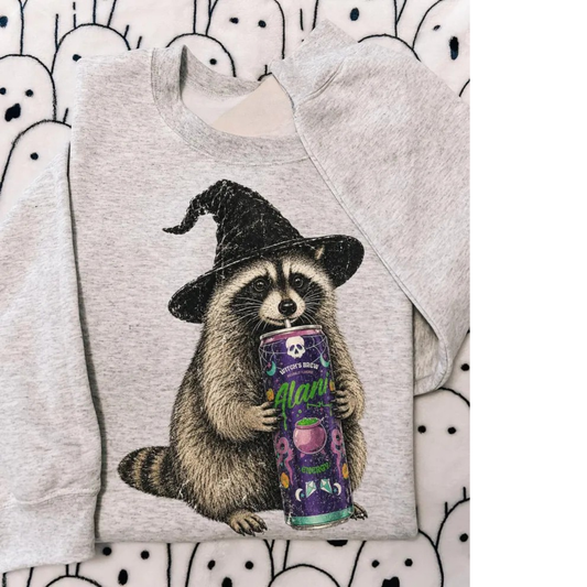 A light heather gray sweatshirt featuring a graphic print of a raccoon in a black witch hat holding a purple can of 'Spooky Magic' candy, laid flat on a white background with a black cartoon ghost pattern.