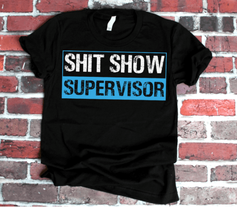 Black t-shirt with 'SHIT SHOW SUPERVISOR' text on a brick wall background