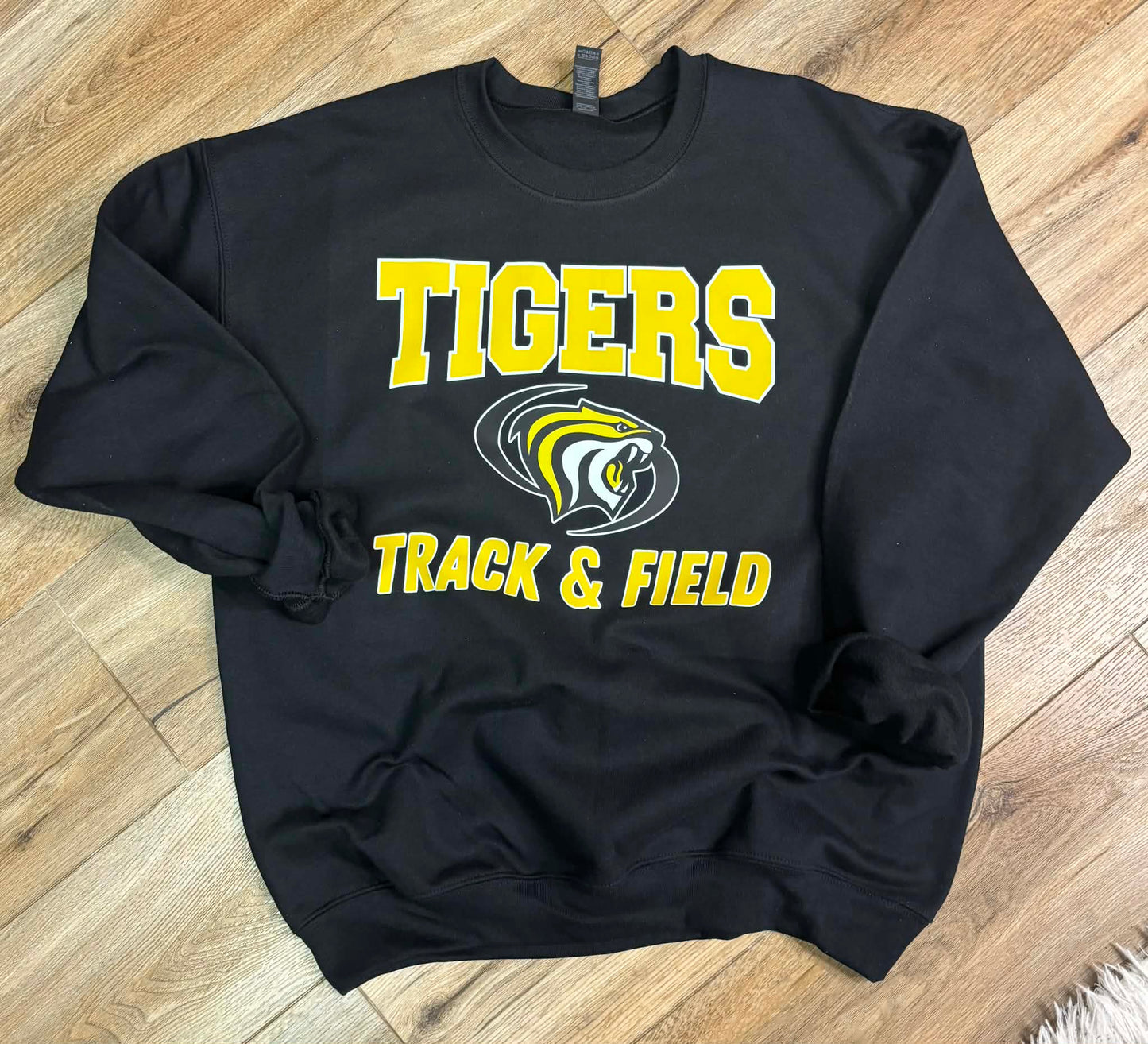 Black sweatshirt with 'Tigers Track & Field' text and logo on a wooden floor.