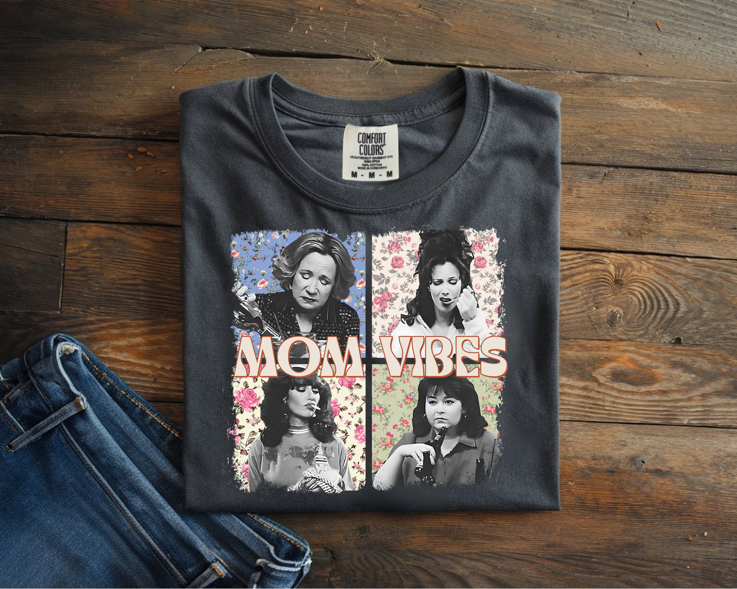 Black t-shirt with 'Mom Vibes' graphic on a wooden surface with jeans.