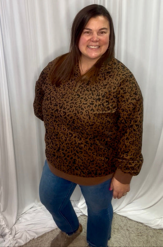 Person wearing a leopard print sweater and blue jeans against a white curtain background