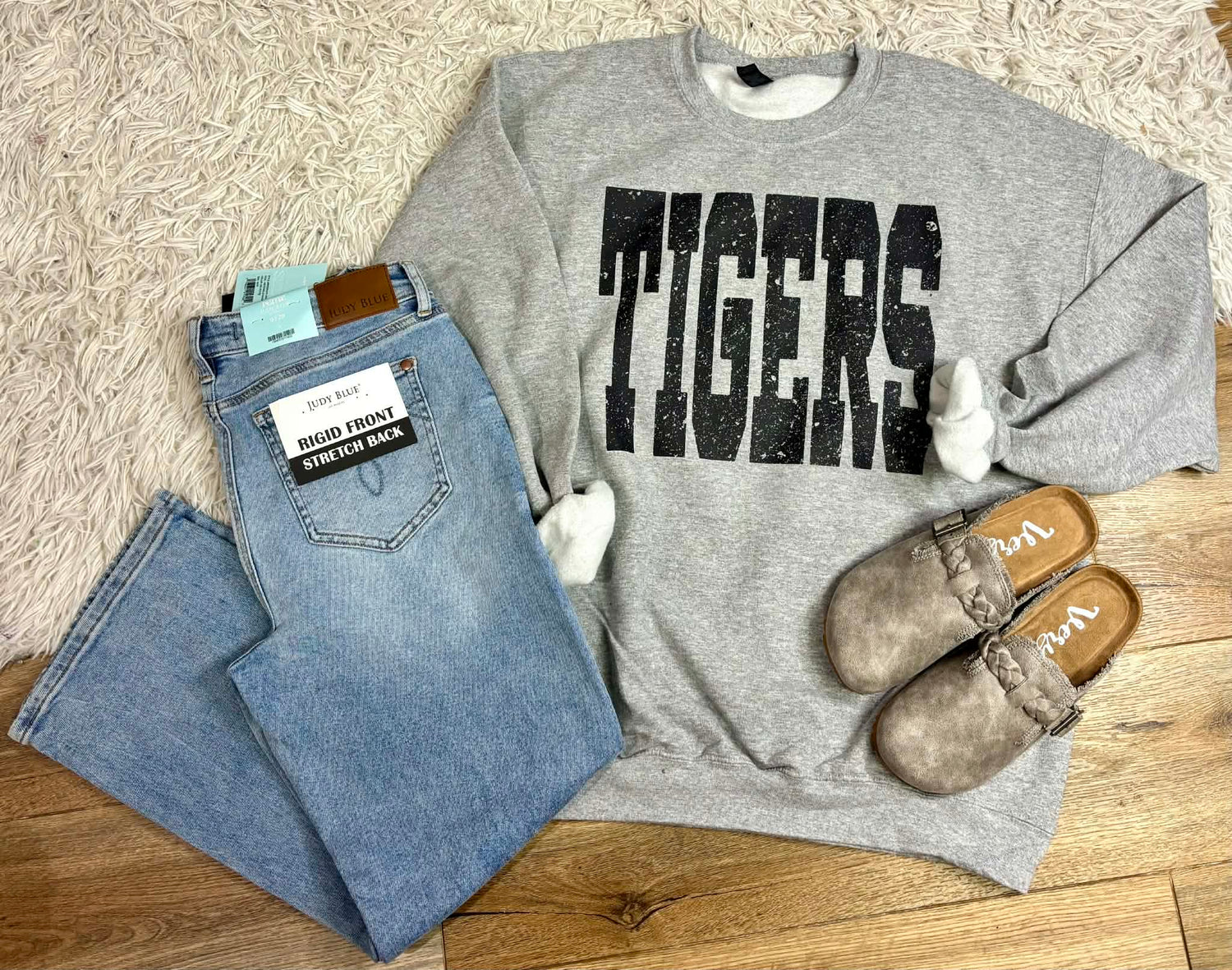Gray sweatshirt with 'TIGERS' print, blue jeans, and brown shoes on a wooden floor.
