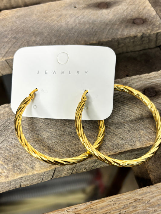 Gold hoop earrings on a wooden surface with a visible brand tag.