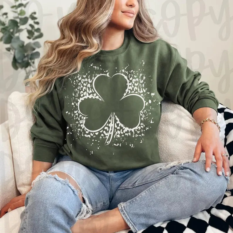 Person wearing a green sweatshirt with a shamrock design, sitting on a couch.