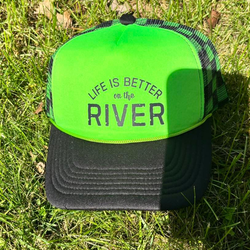 Green and black cap with 'Life is Better on the River' text on grass