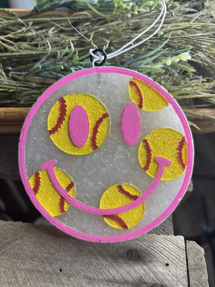 Decorative item with a smiley face made of yellow and pink softball shapes on a clear background.