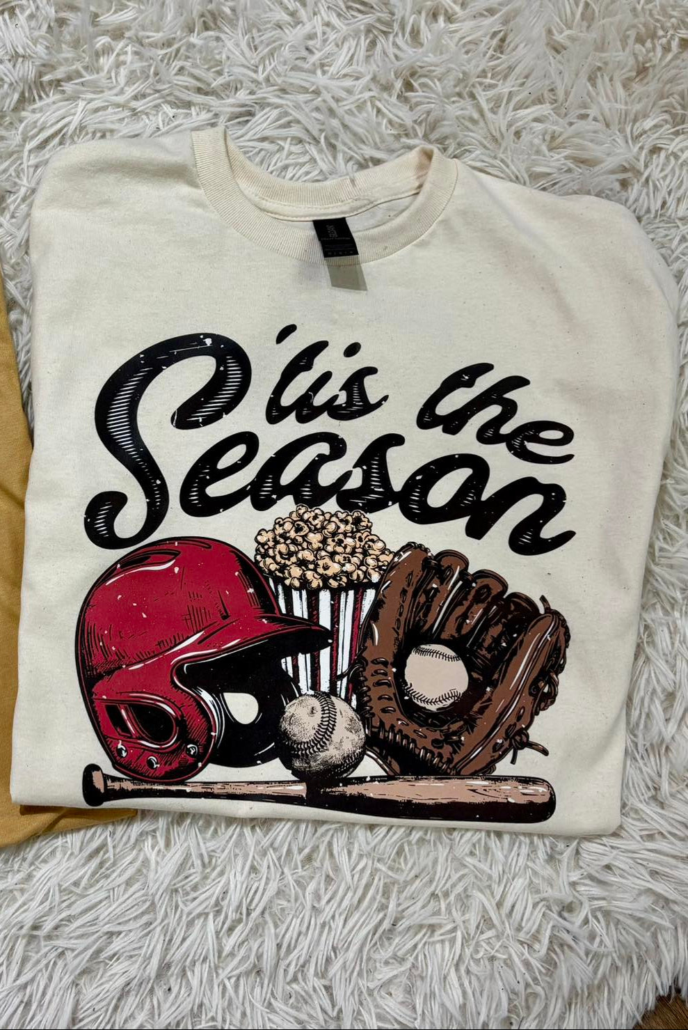 White sweatshirt with sports-themed design and text 'O' is the Season' on a fluffy white surface.