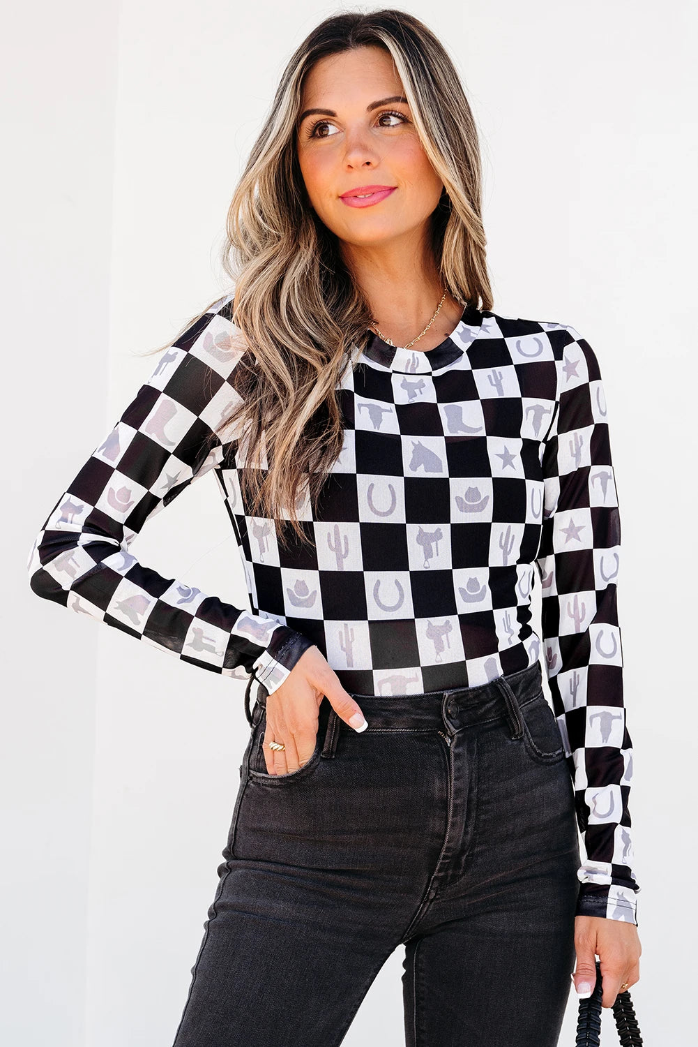 Woman wearing a black and white checkered long-sleeve top with patterned sleeves on a plain background